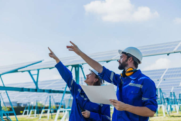 Engineers checking solar panel male and female worker wearing a uniform and safety helmet checking with paper plan on operation of solar panel system at solar station